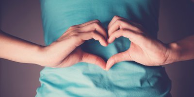 Žena si na břiše drží ruce spojené do tvaru srdce