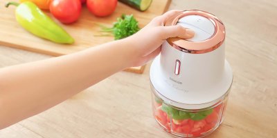 Ruka spouštějící sekáček na potraviny plný rajčat a bazalky