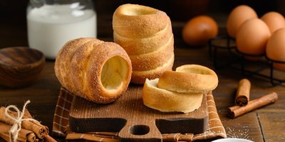 Trdelník na prkénku na stole a kolem ingredience k jeho přípravě