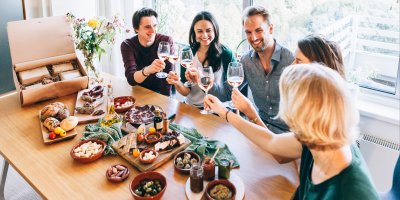 Skupina přátel si připíjí nad stolem plným drobných pochutin