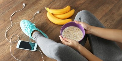 Žena ve cvičebním drží misku s cereáliemi a vedle trs banánů