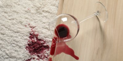Červené víno rozlité na stolku a na koberci, sklenice