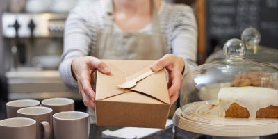 Zaměstnankyně kavárny předává papírový box s dřevěným příborem