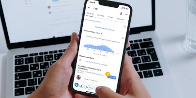 Lidská ruka drží mobilní telefon v pozadí notebook 