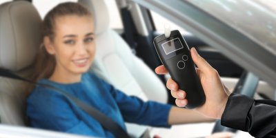 Žena sedí v autě, člověk stojící před autem drží alkohol tester