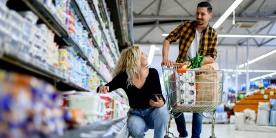 Žena klečí u regálu v supermarketu a dívá se na muže u nákupního vozíku