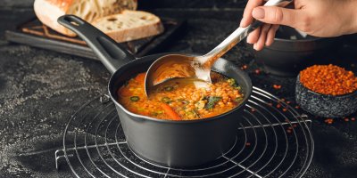 Ruka míchající naběračkou čočku v rendlíku