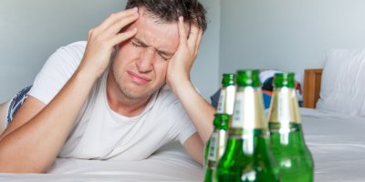 Rozespalý muž se v bolestech dívá na prázdné lahve piva