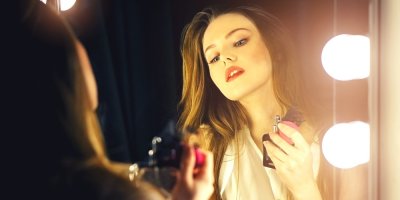 Žena drží parfém v ruce před zrcadlem