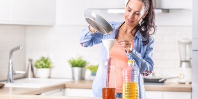 Žena pomocí trychtýře přelévá přepálený olej z pánve do PET láhve