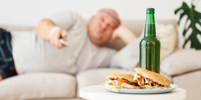Pivo a hamburgery, v pozadí ležící muž na gauči