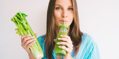 Žena drží řapíkatý celer v celku pije šťávu ze sklenice