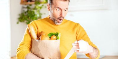 Muž s nákupem v ruce se udiveně kouká na účtenku