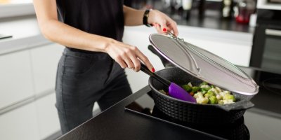 Žena míchá jídlo na pánvi pod pokličkou