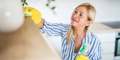 Žena v rukavicích utírá prach nahoře na poličce