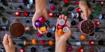 Ruce drží kávu, kávové kapsle a zrnka kávy