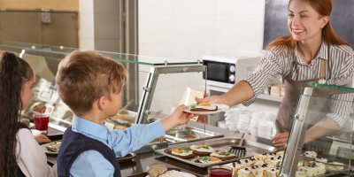 Paní kuchařka v jídelně podává dětem oběd