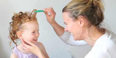 Žena češe vlasy dívce, která má šampon ve vlasech