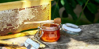 Med ve sklenici a v pozadí plástev a škrabka