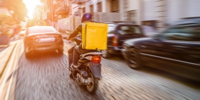 Kurýr se žlutým batohem na zádech jede městem na motorcce