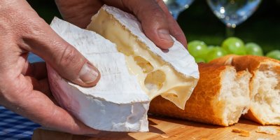 Člověk rozděluje hermelín na dvě poloviny, v pozadí bageta a hroznové víno