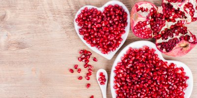 Rozkrojené granátové jablko a zrníčka granátového jablka v miskách ve tvaru srdce