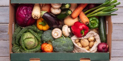 Kartonová bedýnka, ve které jsou brambory, cibule, rajčata, brokolice, houby, papriky, cuketa a další zelenina