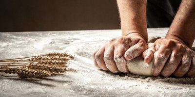 Ruce hnětou těsto na vále, kde je položená pšenice