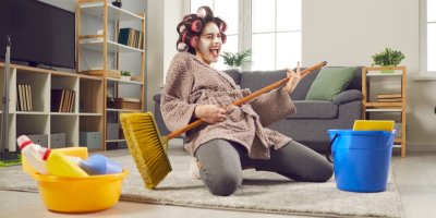 Žena s natáčkami pózuje s koštětem a úklidovými pomůckami