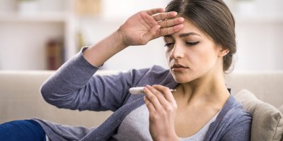 Žena si prohlíží teploměr a drží si čelo
