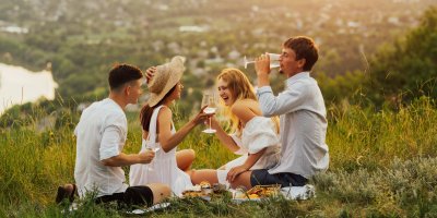 Dva muži a dvě ženy si dávají víno na kopci při západu slunce