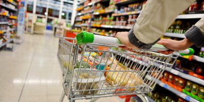 Člověk před sebou tlačí nákupní vozík v uličce supermarketu