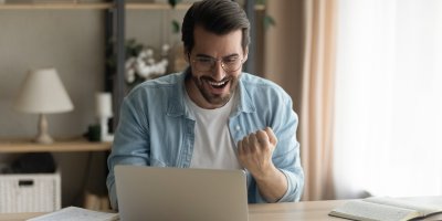 Muž sedí u notebooku a raduje se