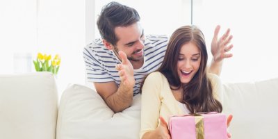 Žena drží růžový dárek, partner stojí za ní