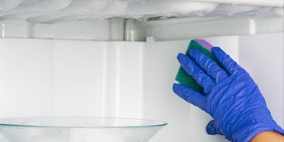 Člověk odmrazuje a čistí mrazák houbičkou