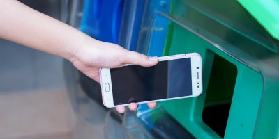 Ruka vhazující starý mobil do kontejneru 