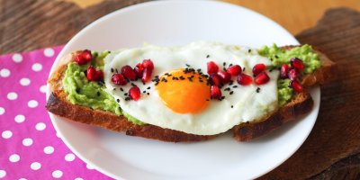 Plátek chleba s avokádovou pomazánkou, volským okem, zrníčky granátového jablka a černým sezamem