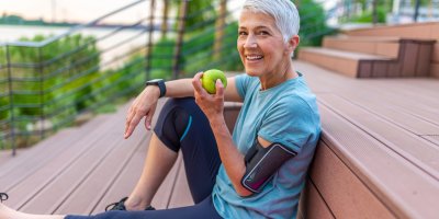 Žena ve sportovním oblečení sedí na zemi a v ruce drží jablko