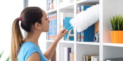 Žena utírá prachovkou knihovnu