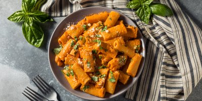 Talíř s těstovinami a rajčatovou omáčkou z vodky, utěrka, bazalka, vidličky