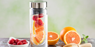 Skleněná lahev na vodu se zásobníkem na ovoce, ve kterém jsou pomeranče a maliny