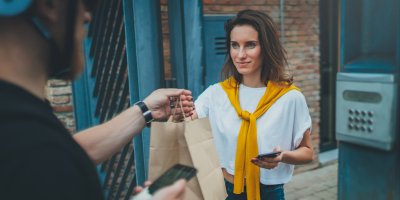 Kurýr předává ženě jídlo v papírové tašce