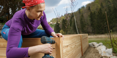 Žena s vrtačkou montuje vyvýšený záhon