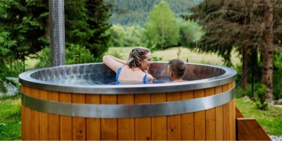 Žena a malý chlapec jsou v dřevěném koupacím sudu, mají výhled na horu a les