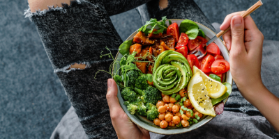 Žena v džínách drží Buddha bowl se salátem, pečené sladké brambory, cizrna, brokolice, zelenina, avokádo, klíčky v rukou