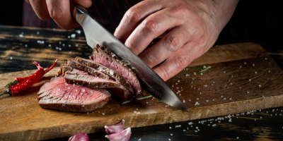 Záběr na ruce, které krájí hovězí maso na dřevěném prkénku