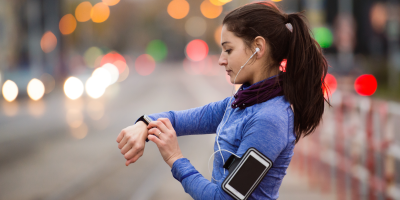 Běžkyně se dívá na sportovní hodinky, na paži má pouzdro na mobil a v uších sluchátka