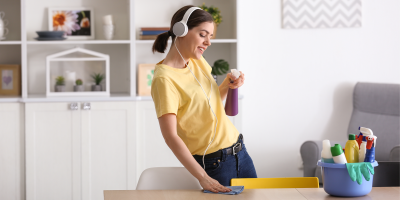 Žena má na hlavě sluchátka a utírá stůl hadrem