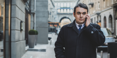 Muž v elegantním oblečení jde po ulici a telefonuje