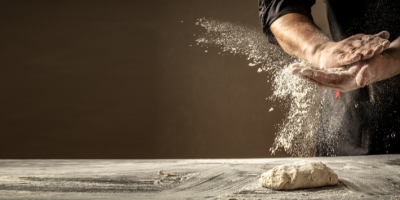 Muž práší mouku na syrové těsto